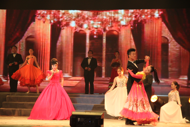 Eine Gruppe von Menschen auf einer Bühne mit Scheinwerfern, Stufen und einem Hintergrundschirm, mit einem Lautsprecher unten, der eine Tanzvorstellung suggeriert.