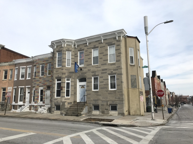Eine Häuserreihe an einer Straßenecke in einem neuen Wohnprojekt in Philadelphia, mit Fenstern, Türen, Geländern, Laternen, Schildern, Fahrzeugen, Bäumen und einem bewölkten Himmel.