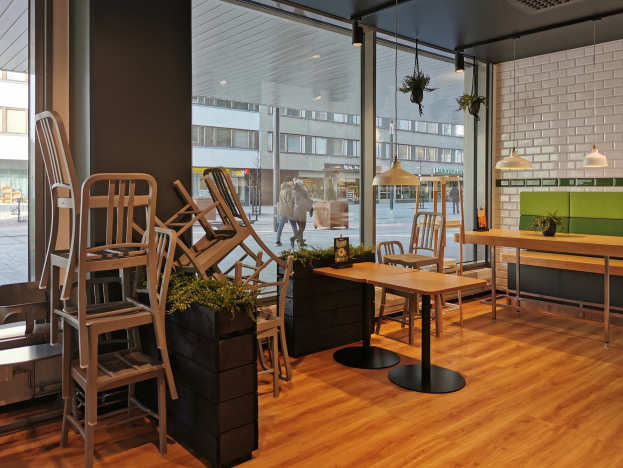 Ein Restaurantinnenraum mit hölzernen Tischen und Stühlen, ein großes Fenster mit Blick auf eine Berliner Straße mit Fußgängern, Gebäuden und Straßenelementen.