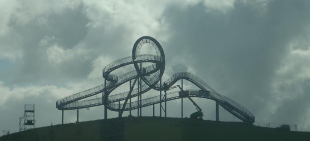 Eine Achterbahn auf dem Gipfel eines Hügels unter einem bewölkten Himmel, mit Stützpfählen und -strukturen.